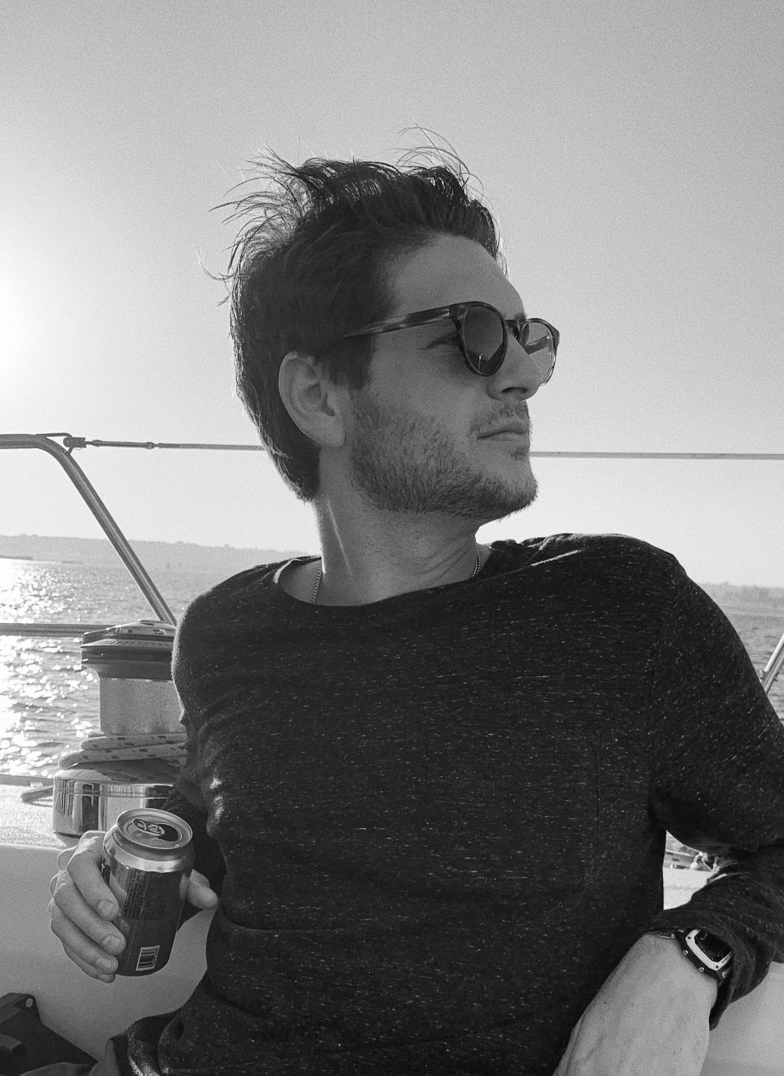 Pierce Gainey sitting on the deck of a sailboat in sunglasses, black and white